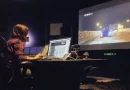 Paola Magrans trabajando en un moderno estudio de sonido frente a una pantalla de televisión gigante.